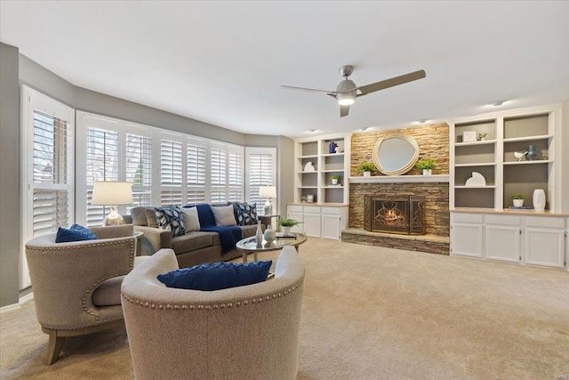 carpeted living room with ceiling fan and a stone fireplace