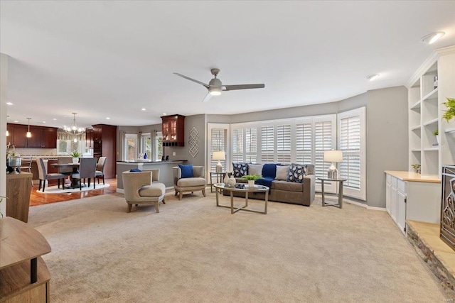 living room featuring recessed lighting, light colored carpet, baseboards, and ceiling fan with notable chandelier