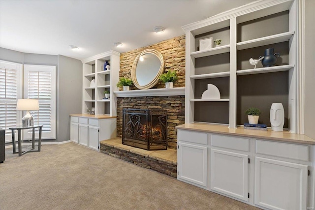 living area featuring built in shelves, light carpet, and a stone fireplace