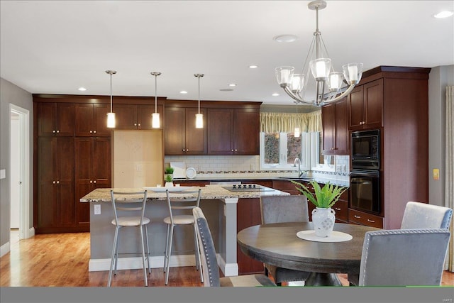 kitchen with decorative backsplash, a sink, a kitchen island, light wood-type flooring, and black appliances