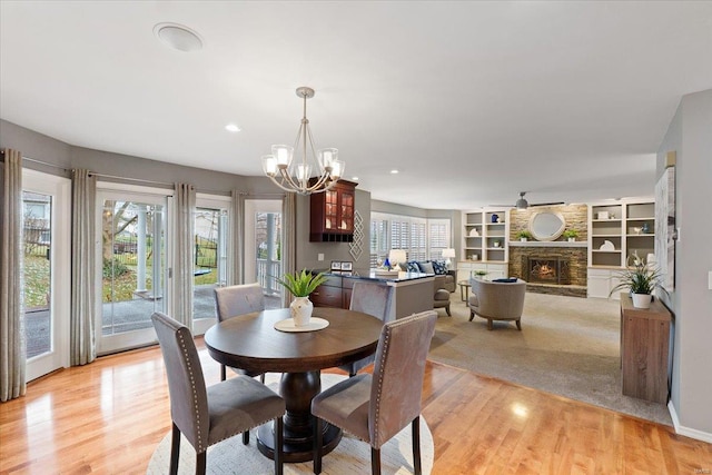 dining room with light wood-style flooring, recessed lighting, a chandelier, and a stone fireplace