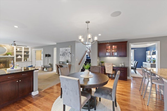 dining space featuring ceiling fan with notable chandelier, a stone fireplace, recessed lighting, and light wood-style floors