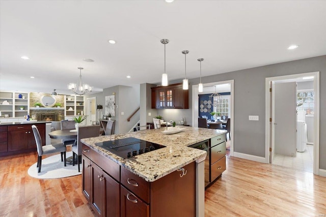 kitchen with a stone fireplace, a kitchen island, black electric cooktop, and light wood-style floors