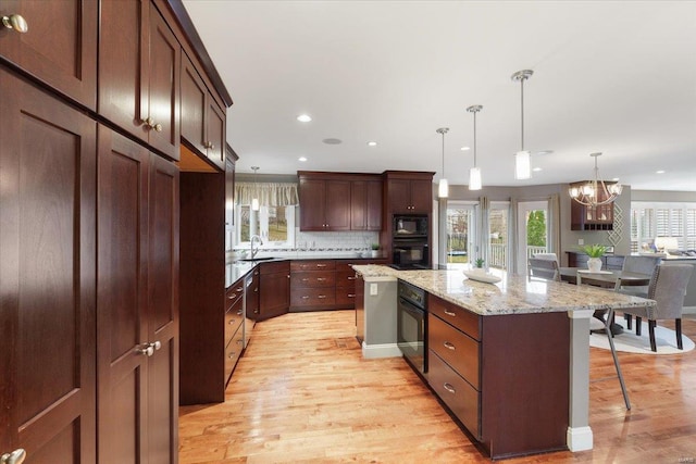 kitchen featuring a breakfast bar, a sink, light wood-type flooring, a center island, and black appliances