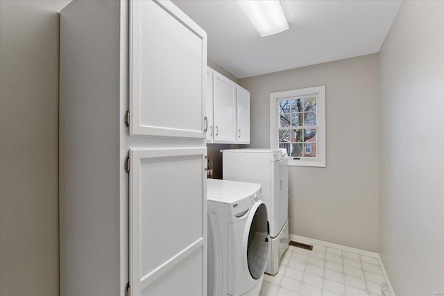 laundry area featuring light floors, washer and clothes dryer, cabinet space, and baseboards