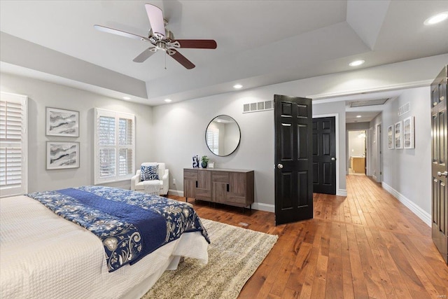 bedroom with baseboards, visible vents, hardwood / wood-style flooring, a tray ceiling, and recessed lighting