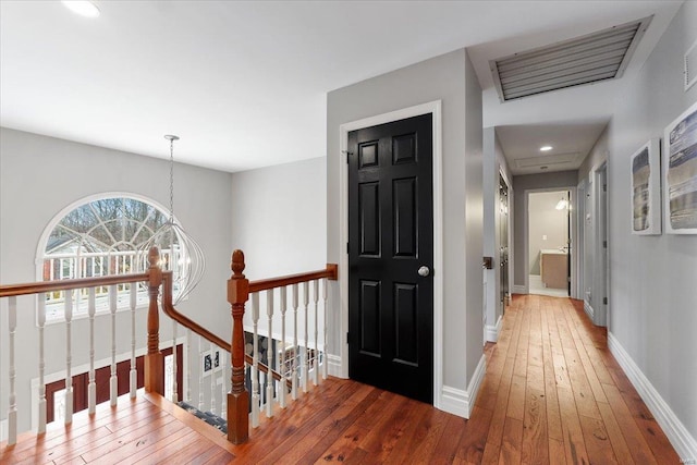 corridor featuring baseboards, visible vents, hardwood / wood-style floors, and an upstairs landing