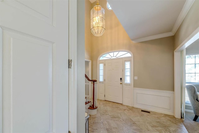 foyer entrance featuring a notable chandelier, a wainscoted wall, a decorative wall, visible vents, and ornamental molding