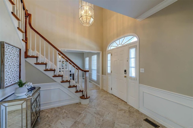 entrance foyer with a decorative wall, visible vents, stairway, wainscoting, and an inviting chandelier