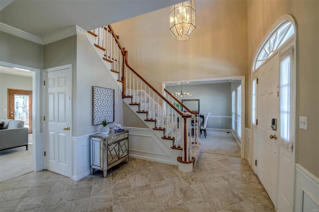 foyer entrance featuring crown molding, a decorative wall, stairway, wainscoting, and a chandelier