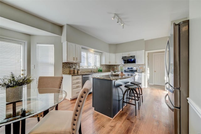 kitchen with stainless steel appliances, a kitchen island, white cabinets, tasteful backsplash, and a kitchen bar