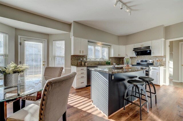 kitchen featuring dark stone counters, white cabinets, appliances with stainless steel finishes, light wood-type flooring, and a sink