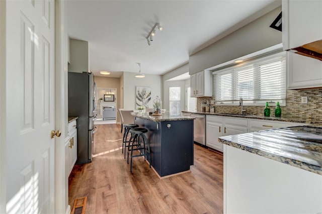 kitchen with white cabinets, decorative backsplash, a kitchen island, stainless steel appliances, and light wood-style floors