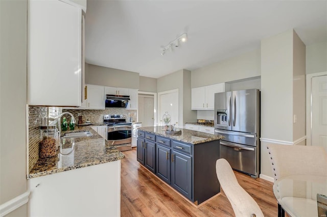 kitchen with decorative backsplash, a kitchen island, light stone counters, stainless steel appliances, and a sink