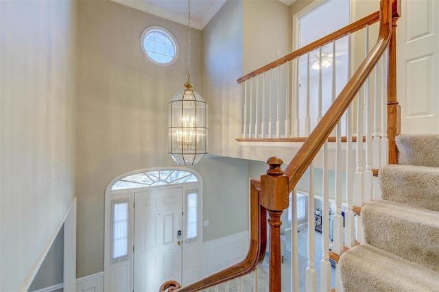 entrance foyer featuring a decorative wall, a wainscoted wall, a notable chandelier, a towering ceiling, and crown molding