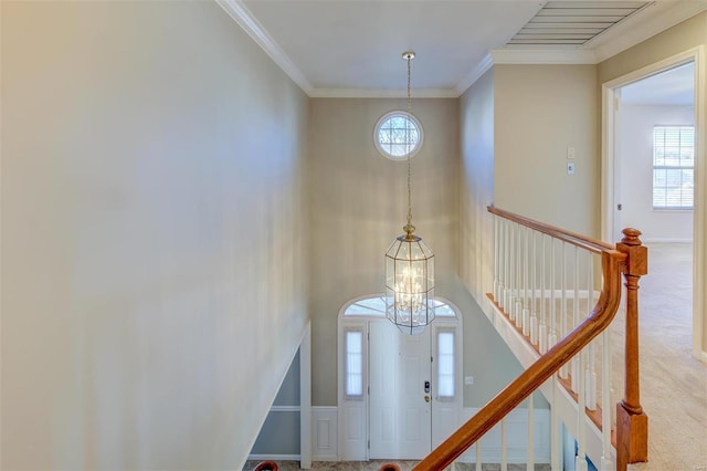 carpeted foyer entrance featuring ornamental molding, visible vents, a notable chandelier, and baseboards