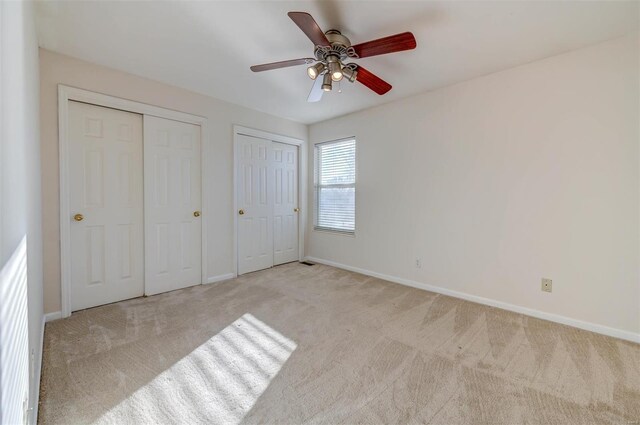 unfurnished bedroom featuring baseboards, carpet flooring, a ceiling fan, and multiple closets