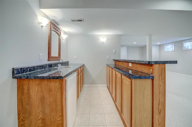 kitchen featuring light tile patterned floors, dark stone counters, dishwasher, a peninsula, and a sink