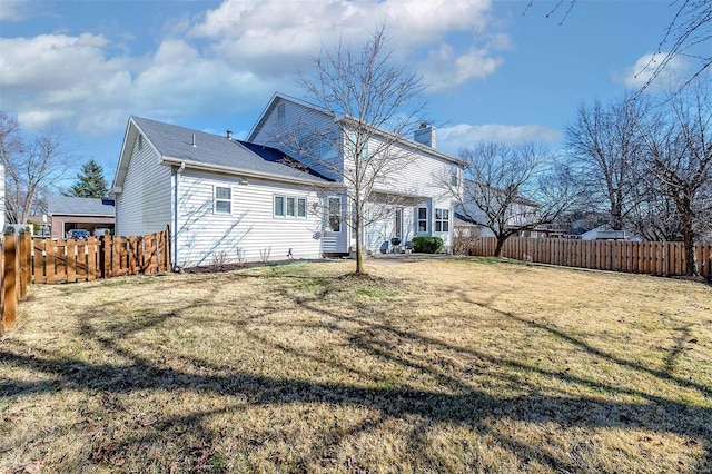 back of house featuring fence private yard, a chimney, and a lawn