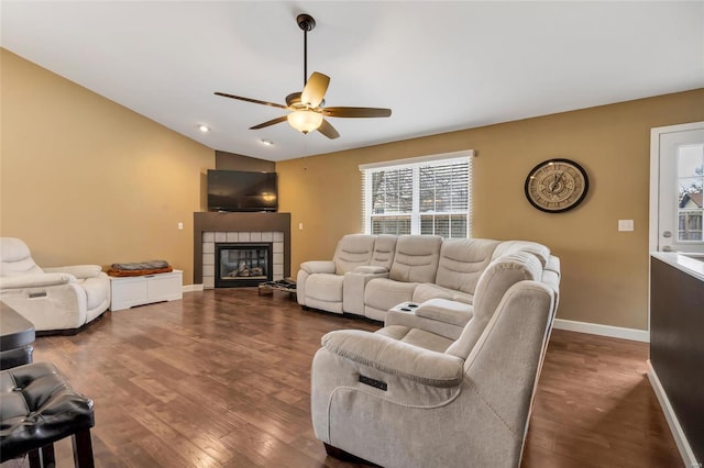 living area with a ceiling fan, baseboards, vaulted ceiling, dark wood-style floors, and a tiled fireplace