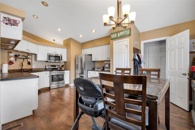 kitchen featuring stainless steel appliances, a sink, visible vents, vaulted ceiling, and dark countertops