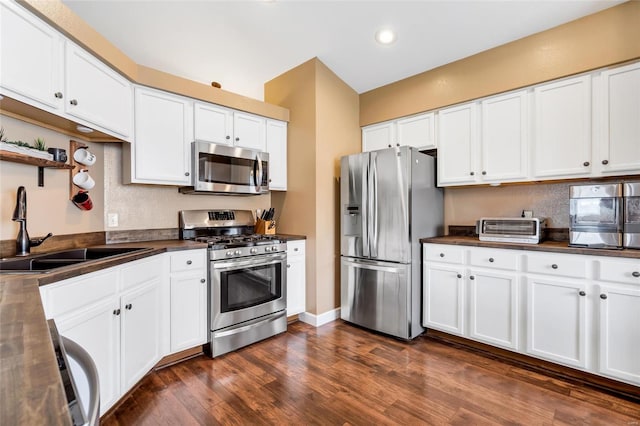 kitchen featuring appliances with stainless steel finishes, dark countertops, a sink, and dark wood finished floors