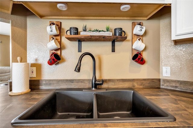 interior details with a textured wall, dark countertops, white cabinets, and a sink