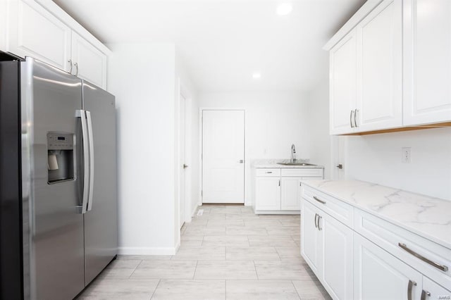 kitchen with light stone counters, recessed lighting, stainless steel fridge, white cabinetry, and a sink