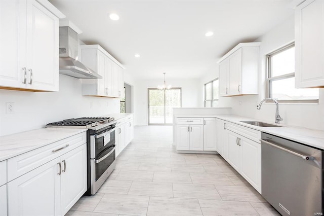 kitchen with a sink, appliances with stainless steel finishes, wall chimney exhaust hood, and white cabinets