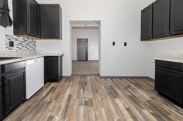 kitchen with light countertops, decorative backsplash, white dishwasher, wood finished floors, and dark cabinets