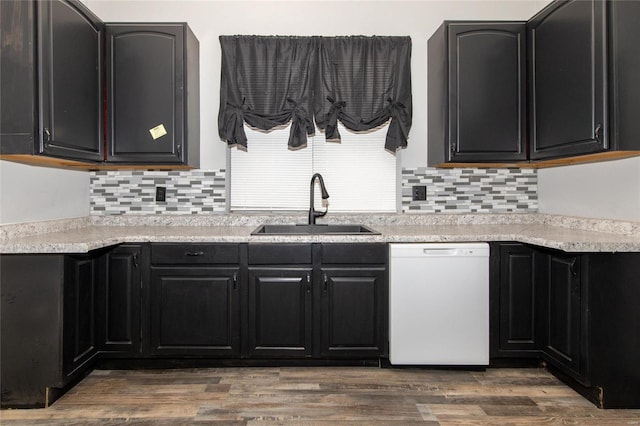 kitchen with wood finished floors, white dishwasher, a sink, and dark cabinets