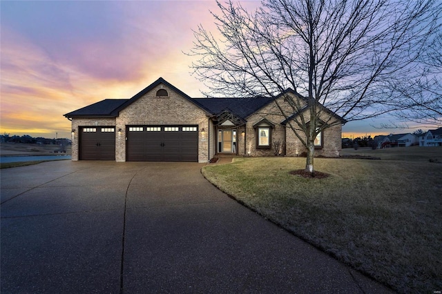 french provincial home with a garage, a lawn, concrete driveway, and brick siding