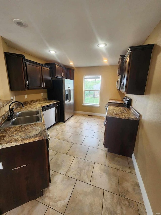 kitchen with dark brown cabinetry, light tile patterned floors, baseboards, stainless steel appliances, and a sink