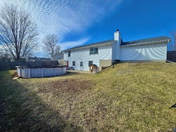 back of property featuring a covered pool, a chimney, fence, and a lawn