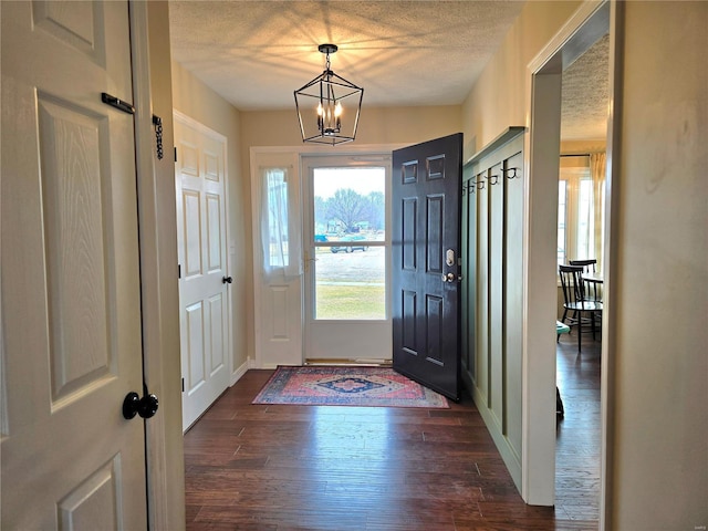 entryway with baseboards, a textured ceiling, a chandelier, and dark wood-type flooring