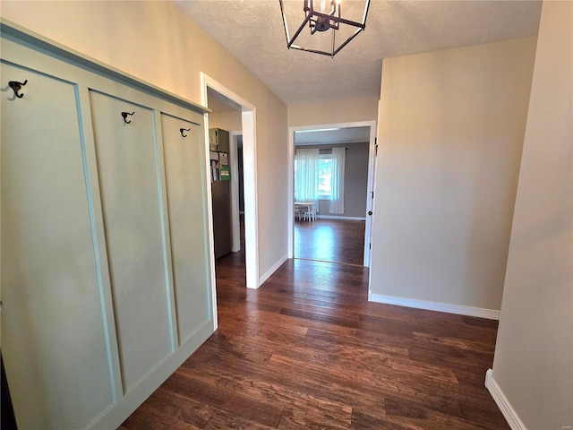 hall with an inviting chandelier, baseboards, dark wood finished floors, and a textured ceiling