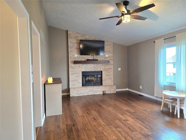 unfurnished living room with visible vents, a brick fireplace, vaulted ceiling, a textured ceiling, and wood finished floors