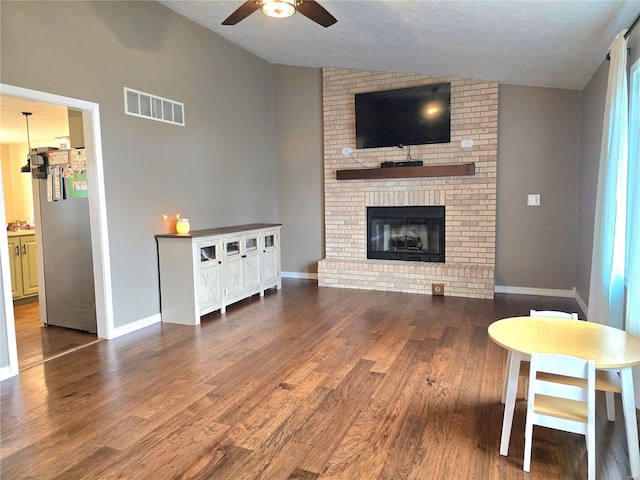 living room featuring baseboards, visible vents, wood finished floors, vaulted ceiling, and a fireplace