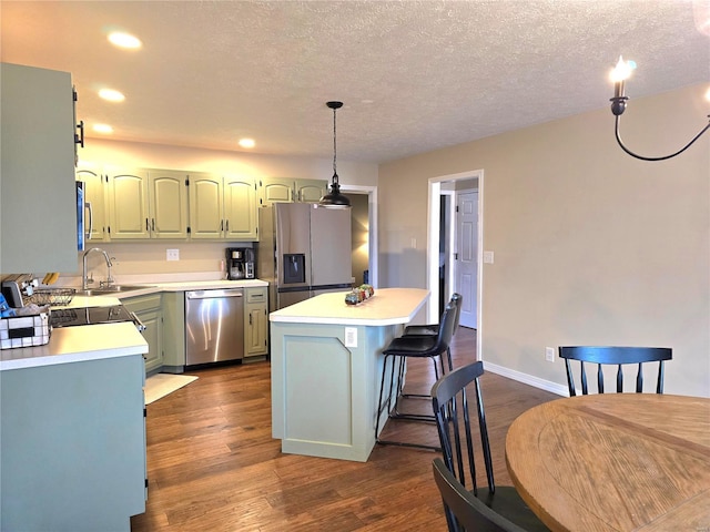 kitchen with a sink, a kitchen island, light countertops, appliances with stainless steel finishes, and dark wood-style floors