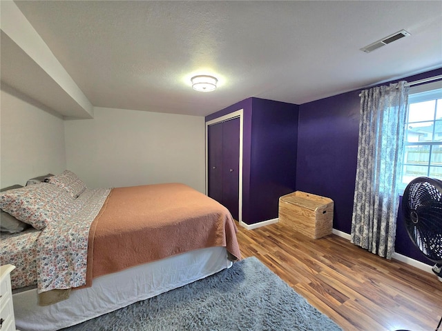 bedroom with a textured ceiling, wood finished floors, visible vents, baseboards, and a closet