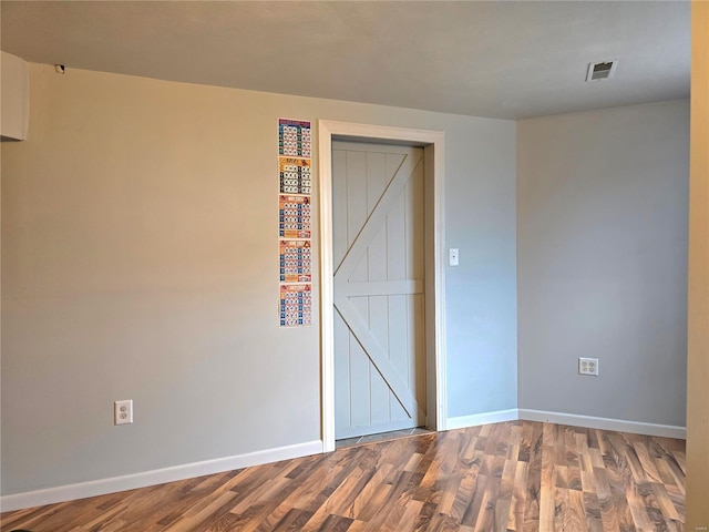 empty room featuring a barn door, wood finished floors, visible vents, and baseboards