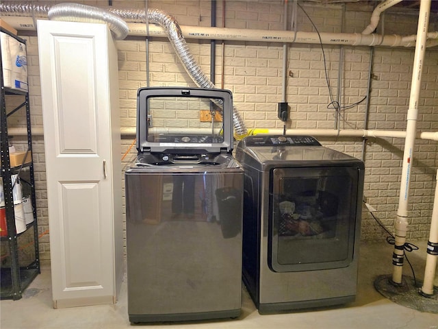 washroom with laundry area, brick wall, and washer and dryer