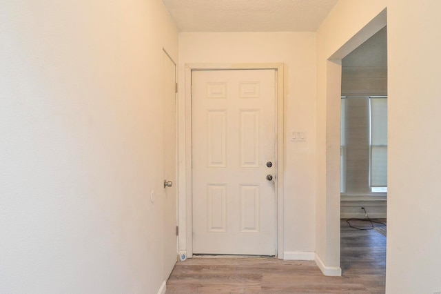 corridor featuring light wood-style flooring, baseboards, and a textured ceiling