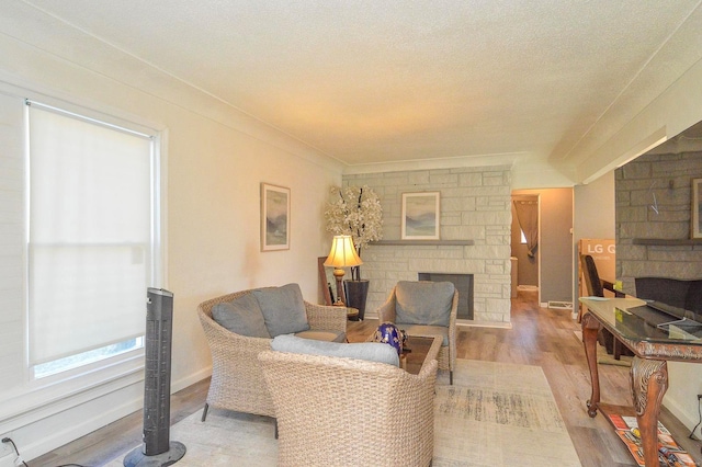 living room featuring crown molding, a fireplace, a textured ceiling, wood finished floors, and baseboards