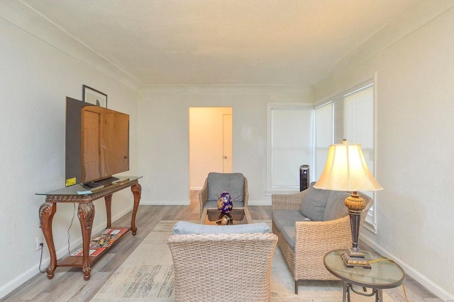 sitting room with light wood-style floors, baseboards, and crown molding