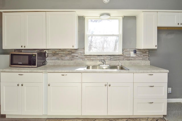 kitchen with stainless steel microwave, a sink, decorative backsplash, and white cabinetry