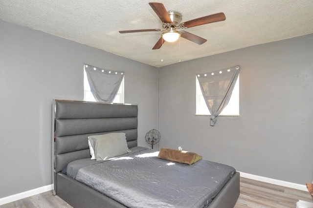 bedroom with light wood-style flooring, baseboards, ceiling fan, and a textured ceiling