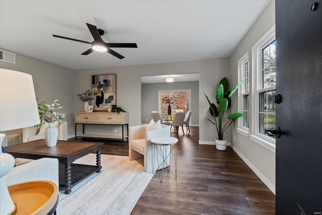 living room featuring a ceiling fan, visible vents, baseboards, and wood finished floors