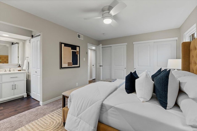 bedroom with baseboards, visible vents, ensuite bathroom, two closets, and a sink