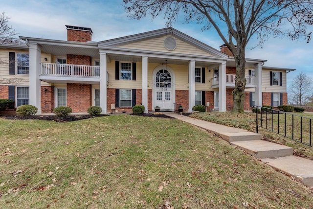 neoclassical / greek revival house with brick siding, a chimney, a front lawn, and fence